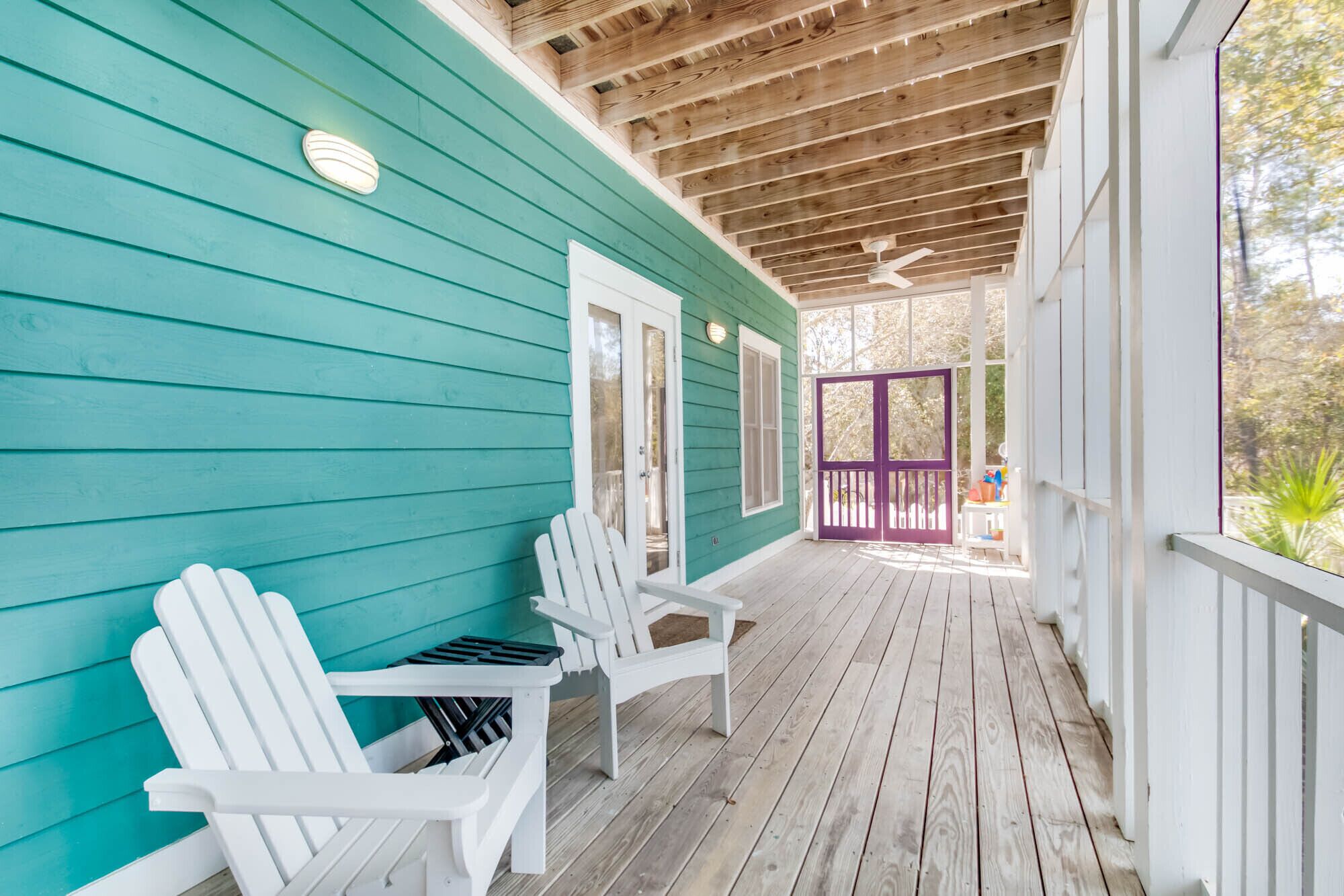 A wooden deck with two white Adirondack chairs and a teal house.