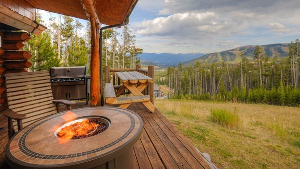 Un terrazzo in legno con un braciere, posti a sedere all'aperto e vista su una foresta e montagne.