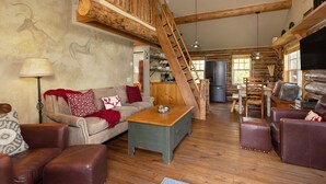 L'interno accogliente di una baita rustica, con una scala in legno, un divano, un tavolo da pranzo e un angolo cottura.