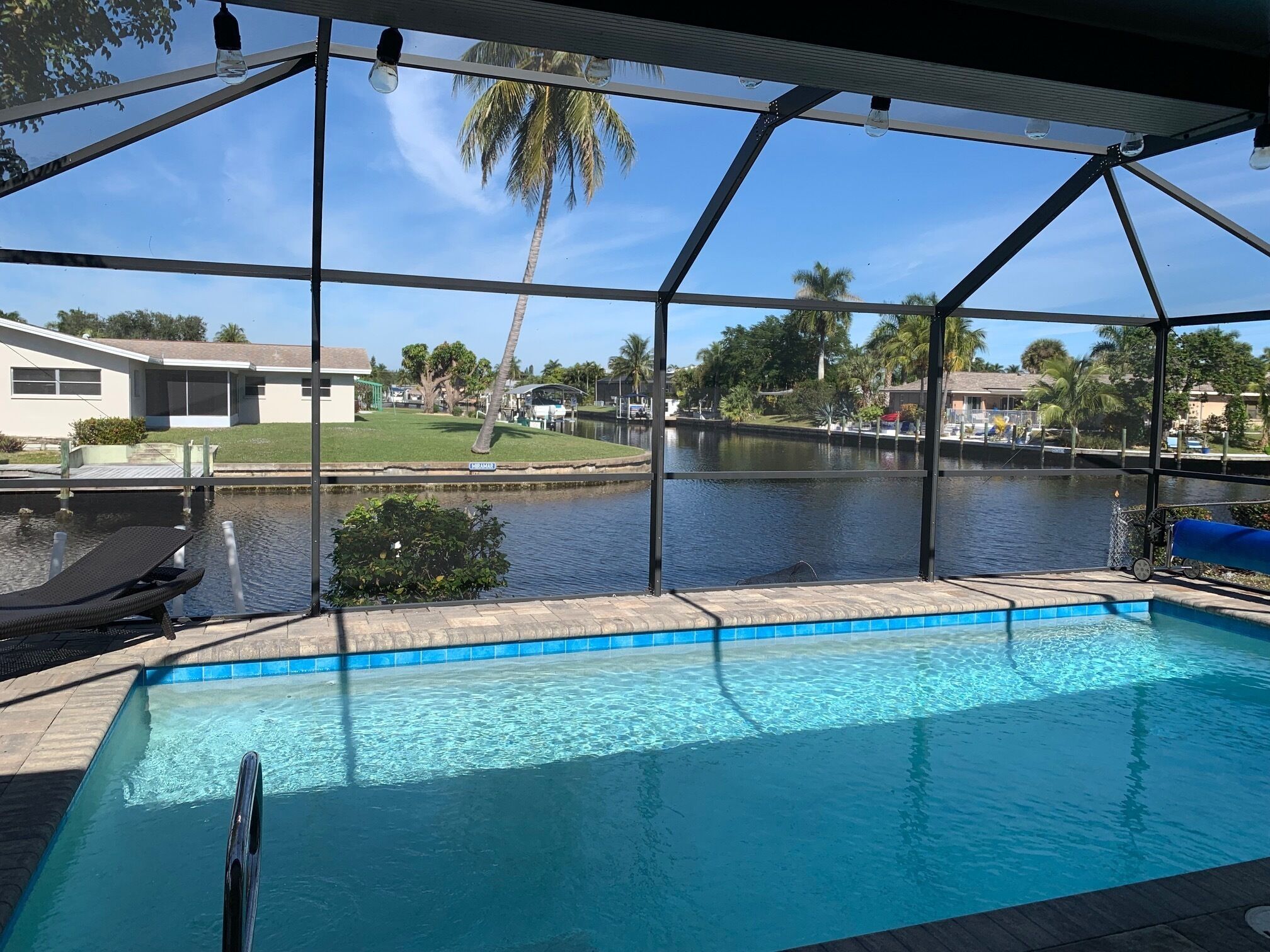 Une piscine avec vue sur un lac et des palmiers, entourée d’une zone couverte dotée d’un toit et de poutres métalliques.