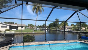Une piscine avec vue sur un lac et des palmiers, entourée d’une zone couverte dotée d’un toit et de poutres métalliques.