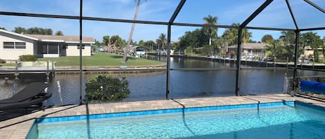 En swimmingpool med utsikt över en sjö och palmer, omgiven av ett takförsett område med tak och metallbalkar.