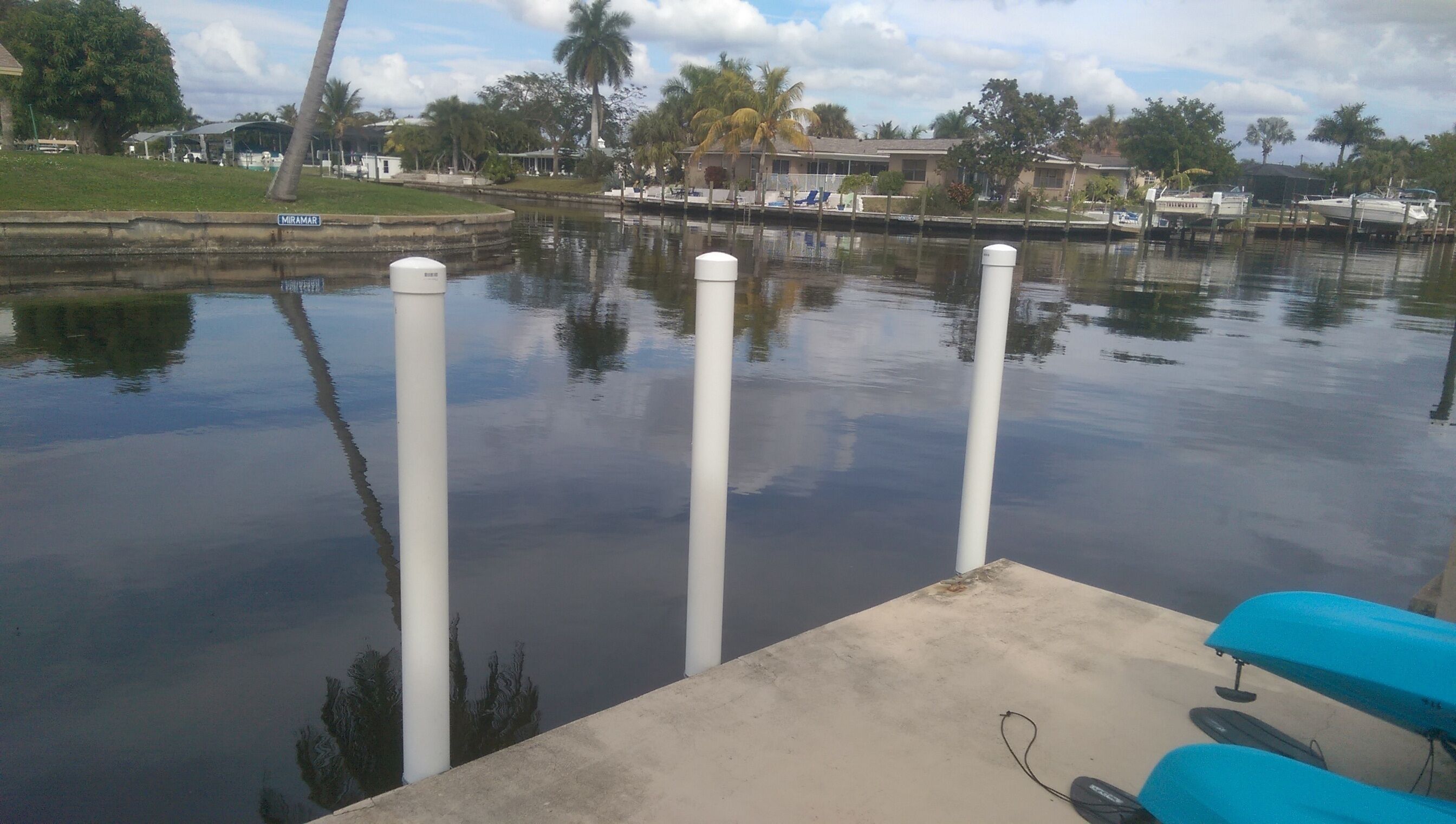 A calm water body with a dock, a concrete platform, and a row of houses in the background.