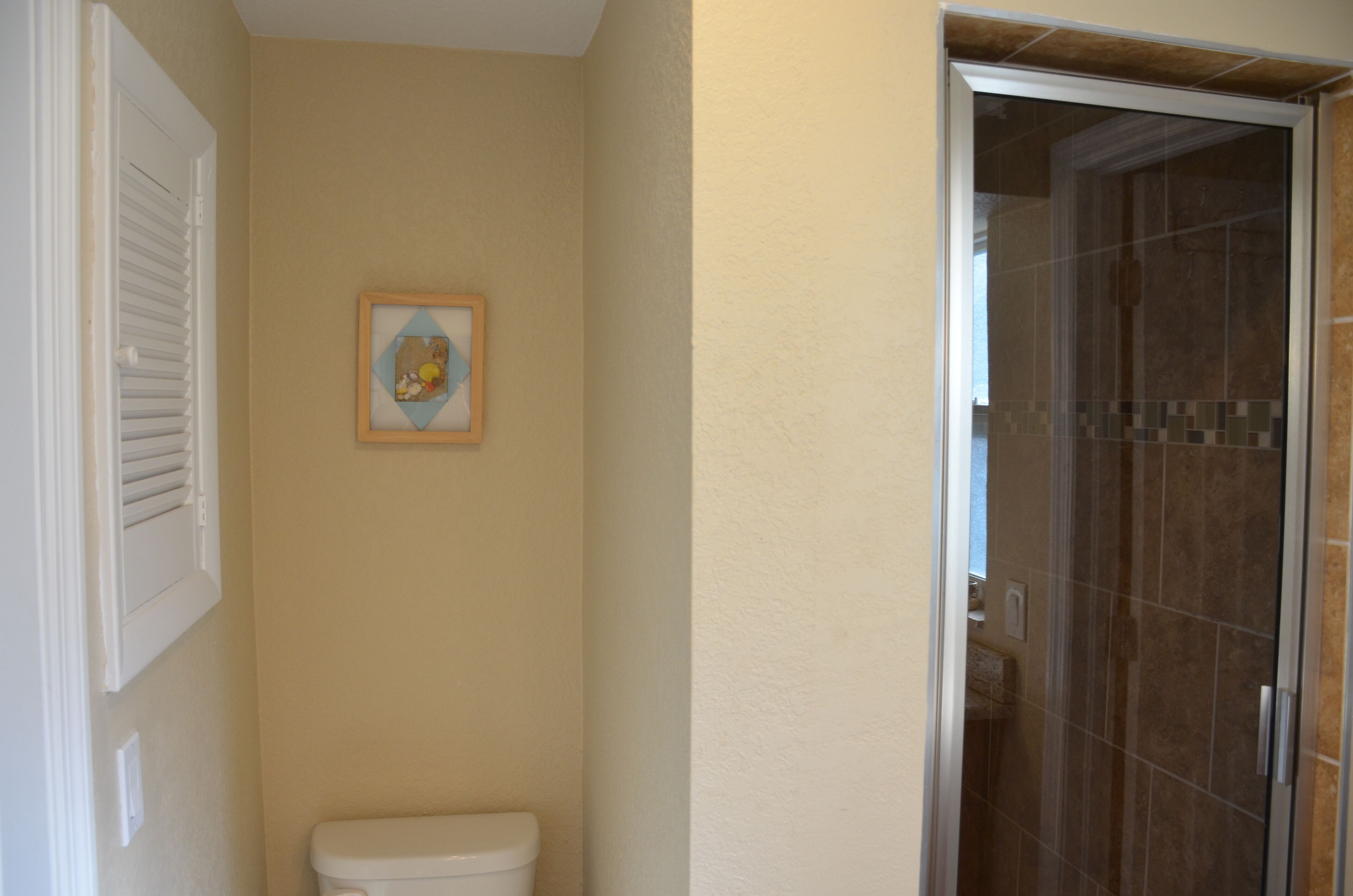 A bathroom with a toilet, a framed picture on the wall, and a shower area with tiled walls.