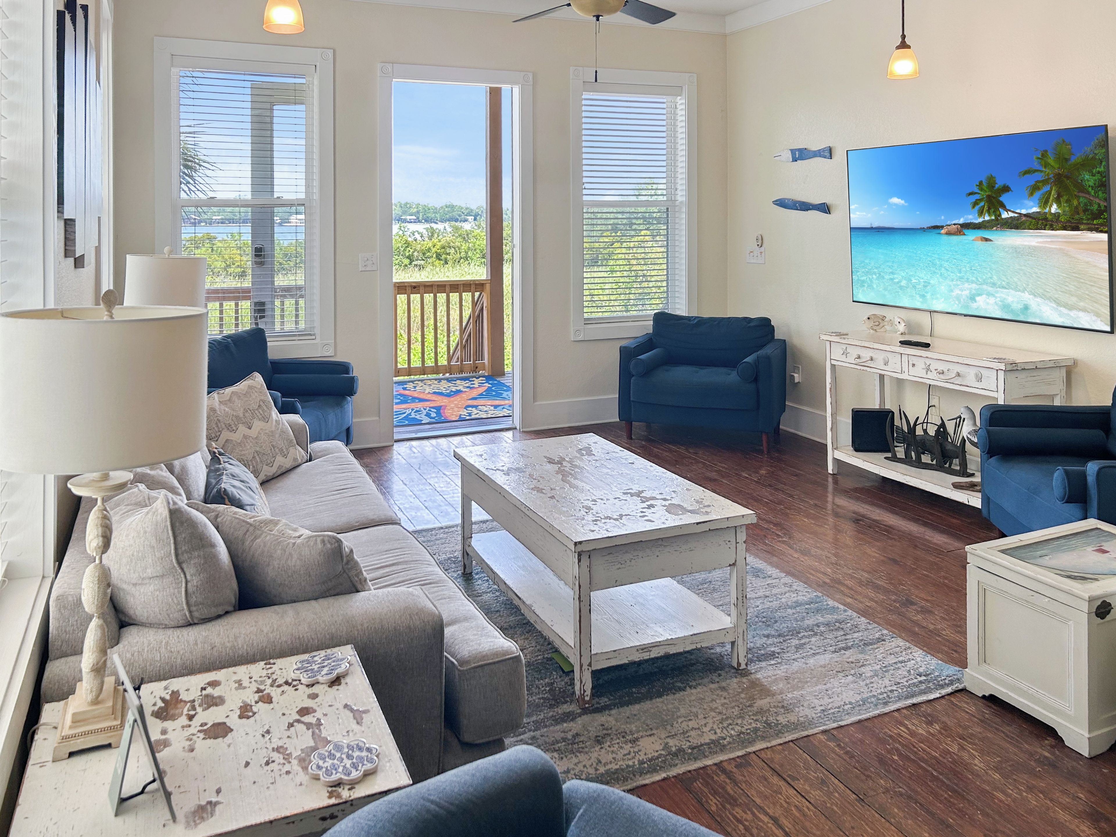 Un salon comprenant un canapé, des fauteuils, une table basse, un téléviseur et une vue sur la plage, visible à travers les fenêtres.