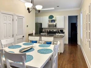 A compact kitchen with white cabinets, a microwave, and a stove. There is a dining table with blue placemats and a fish on it.
