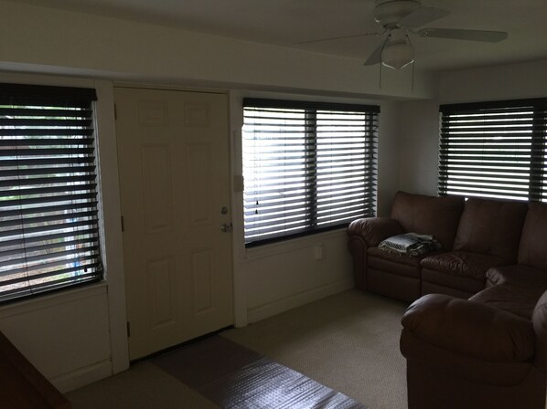 A living room with a brown leather sofa, a ceiling fan, and a door with a window.
