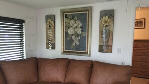 A brown leather sofa in a room with white walls, a door, and three framed floral paintings.