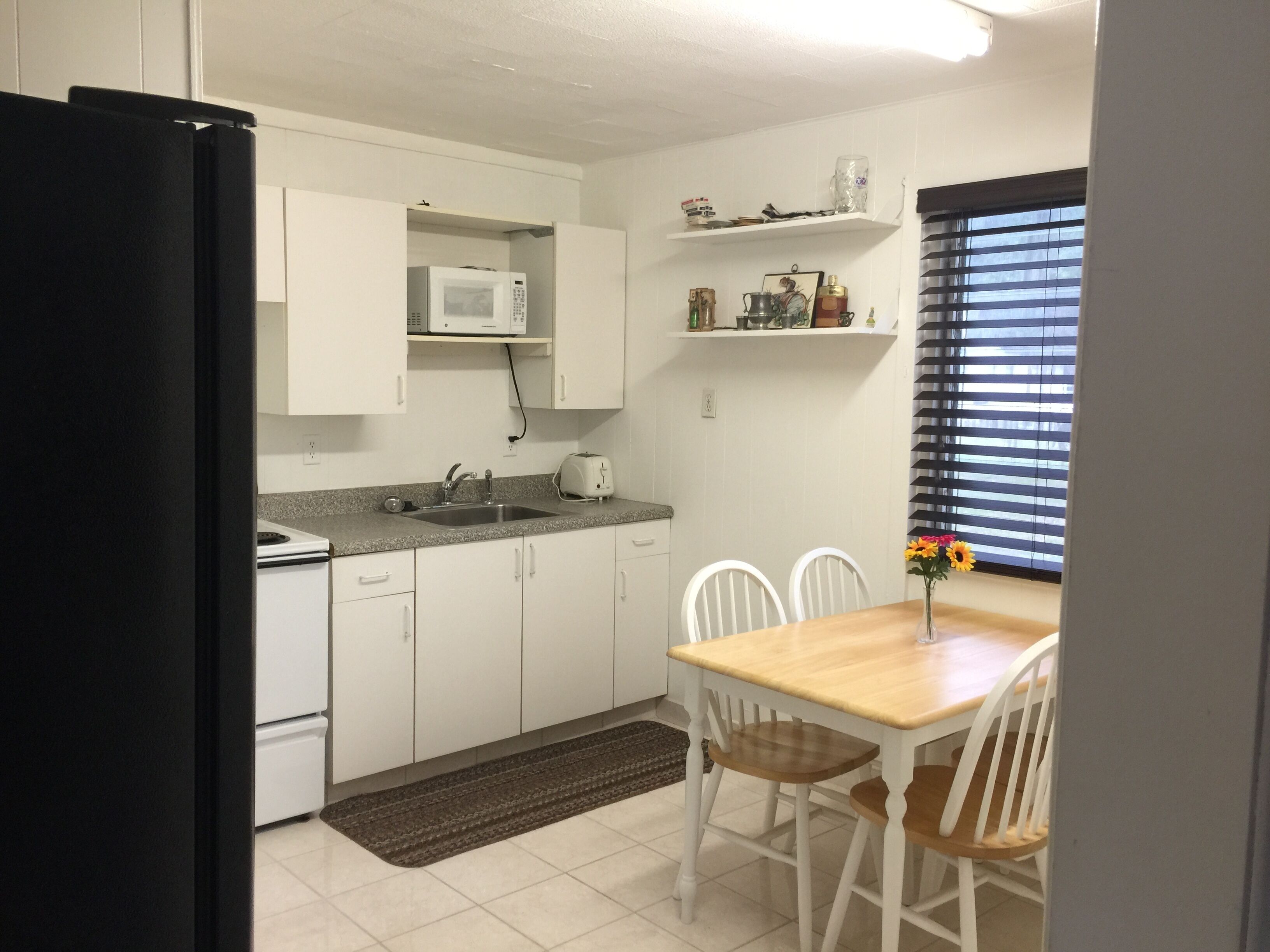 A compact kitchen with white cabinets, a microwave, a toaster, and a dining table with chairs.
