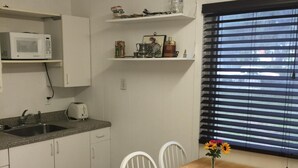 A compact kitchen with white cabinets, a microwave, a sink, and a dining area with a wooden table and white chairs.
