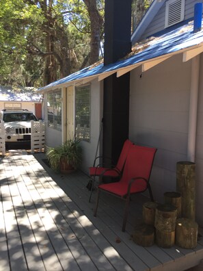 A covered porch with a red chair, wooden logs, and a vehicle parked in the background.