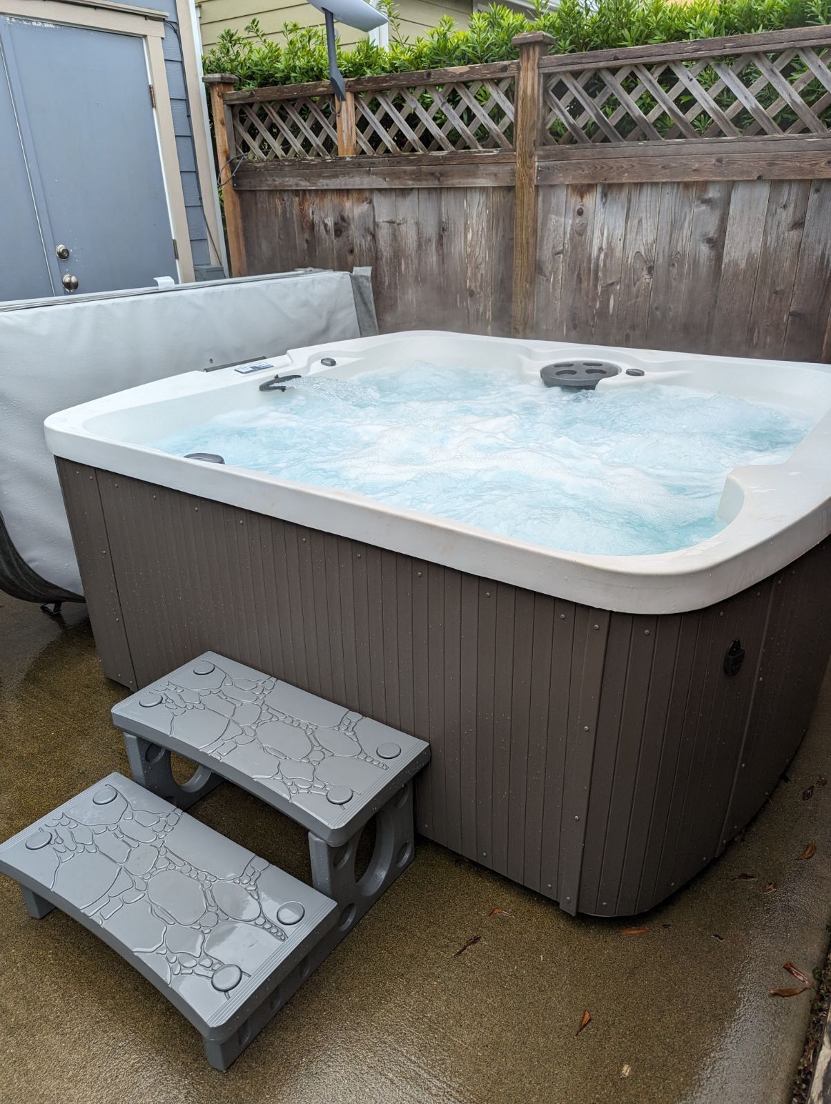 A hot tub with steps, surrounded by a wooden fence and a covered patio area.