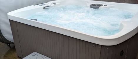 A hot tub with steps, surrounded by a wooden fence and a covered patio area.
