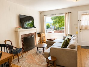 A living room with a fireplace, a television, a sofa, a dining table, and a view of the outdoors. - CUTE and COMFORTABLE, in a quaint location, Central AC, DOG friendly (Hood River)