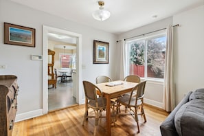 A dining area with a wooden table and wicker chairs, a window with curtains, and a view of trees outside.