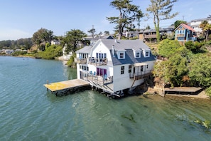 A houseboat with a deck and outdoor seating, docked at a pier.