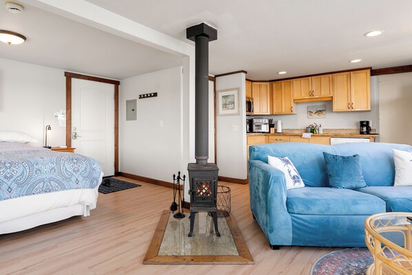 A room with a bed, a blue sofa, a kitchen area, and a fireplace.