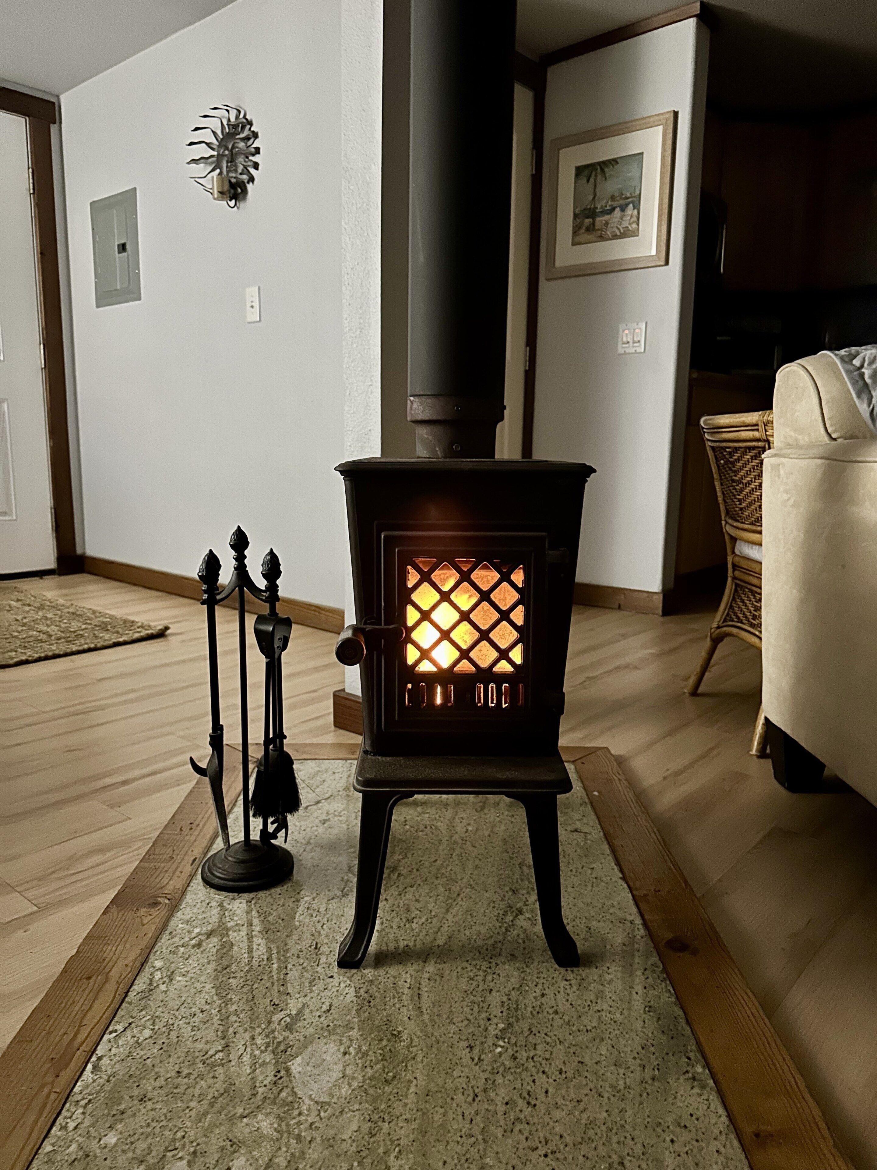 Un poêle à bois doté d’une porte en verre à motifs losangés, d’un socle noir et d’un élément décoratif en métal fixé au mur.