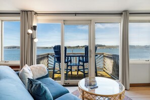 A room with a sofa, a glass table, and a view of a dock and water.