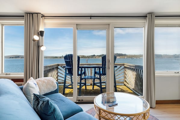 A room with a sofa, a glass table, and a view of a dock and water.