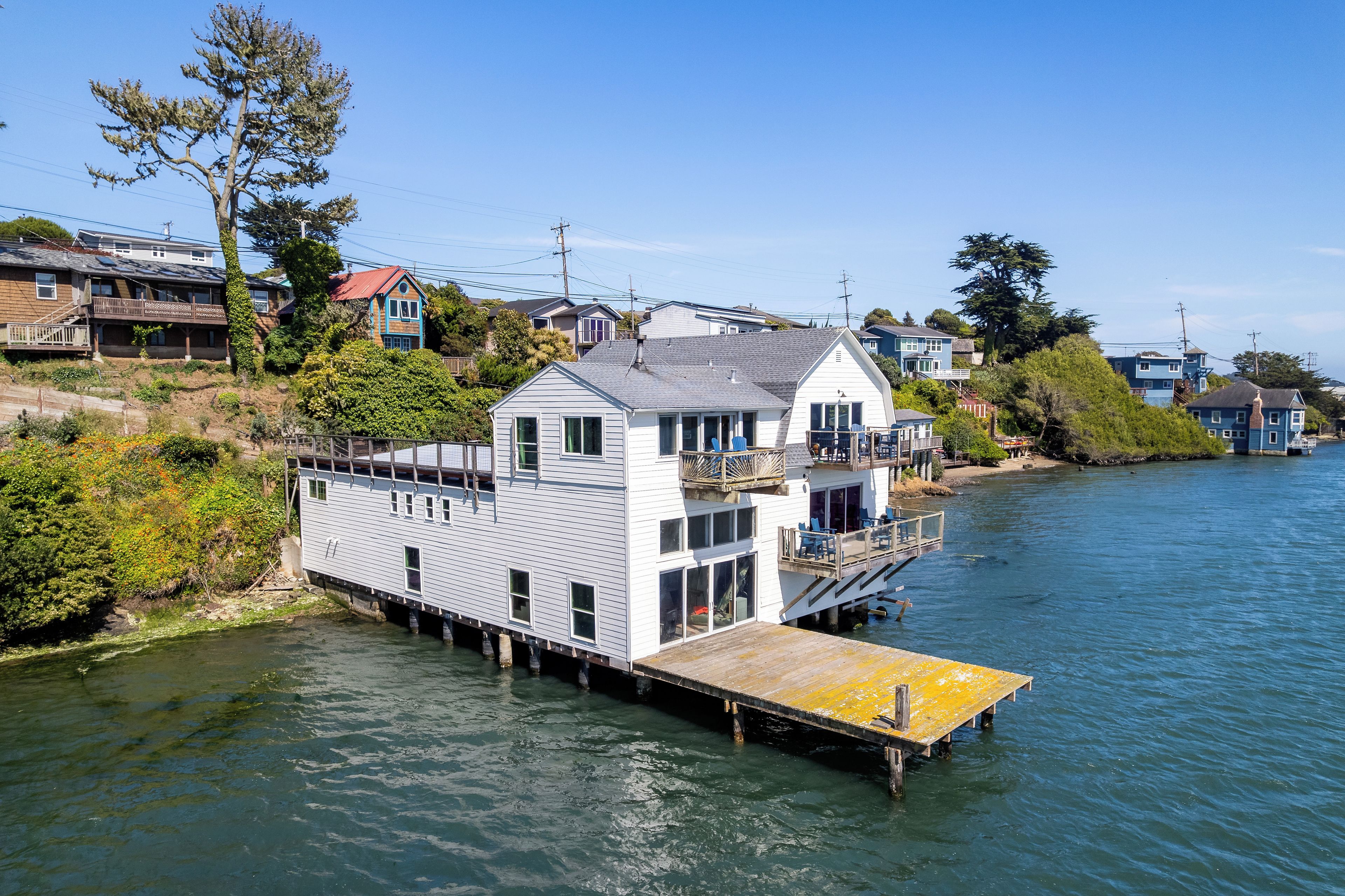 A houseboat with a deck and a small dock, surrounded by water and greenery.