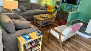 A cozy living room with a green wall, a television, a bookshelf, and a window with curtains. - Four Blocks To Beach & Boardwalk  + Pet Friendly (Ocean City)