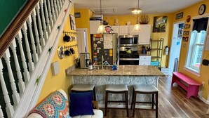 A kitchen with a central island, white cabinets, and a dining area with a white sofa and blue cushions. - Four Blocks To Beach & Boardwalk  + Pet Friendly (Ocean City)