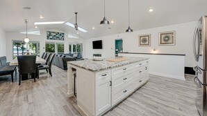 A modern kitchen with white cabinetry, a large island, and a dining area with a sofa and chairs.