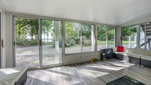 A sunlit room with large sliding glass doors, a wicker sofa, a small table, and a view of a landscaped garden.