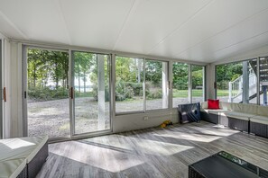 Quarto iluminado pelo sol com grandes portas de vidro deslizantes, um sofá de vime, uma mesa pequena e vista para um jardim ajardinado.