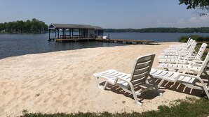 A beach with white lounge chairs and a wooden dock extending into the water.