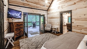 A log cabin room with a bed, a TV, a wooden dresser, and a dining area with a table and chairs. - Elegant Couples Cabin, Magnolia Design, 5-Star Amenities (Broken Bow)