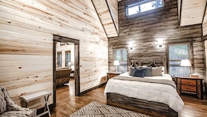 A bedroom with a large bed, wooden walls, a skylight, and a view of the outdoors. - Elegant Couples Cabin, Magnolia Design, 5-Star Amenities (Broken Bow)
