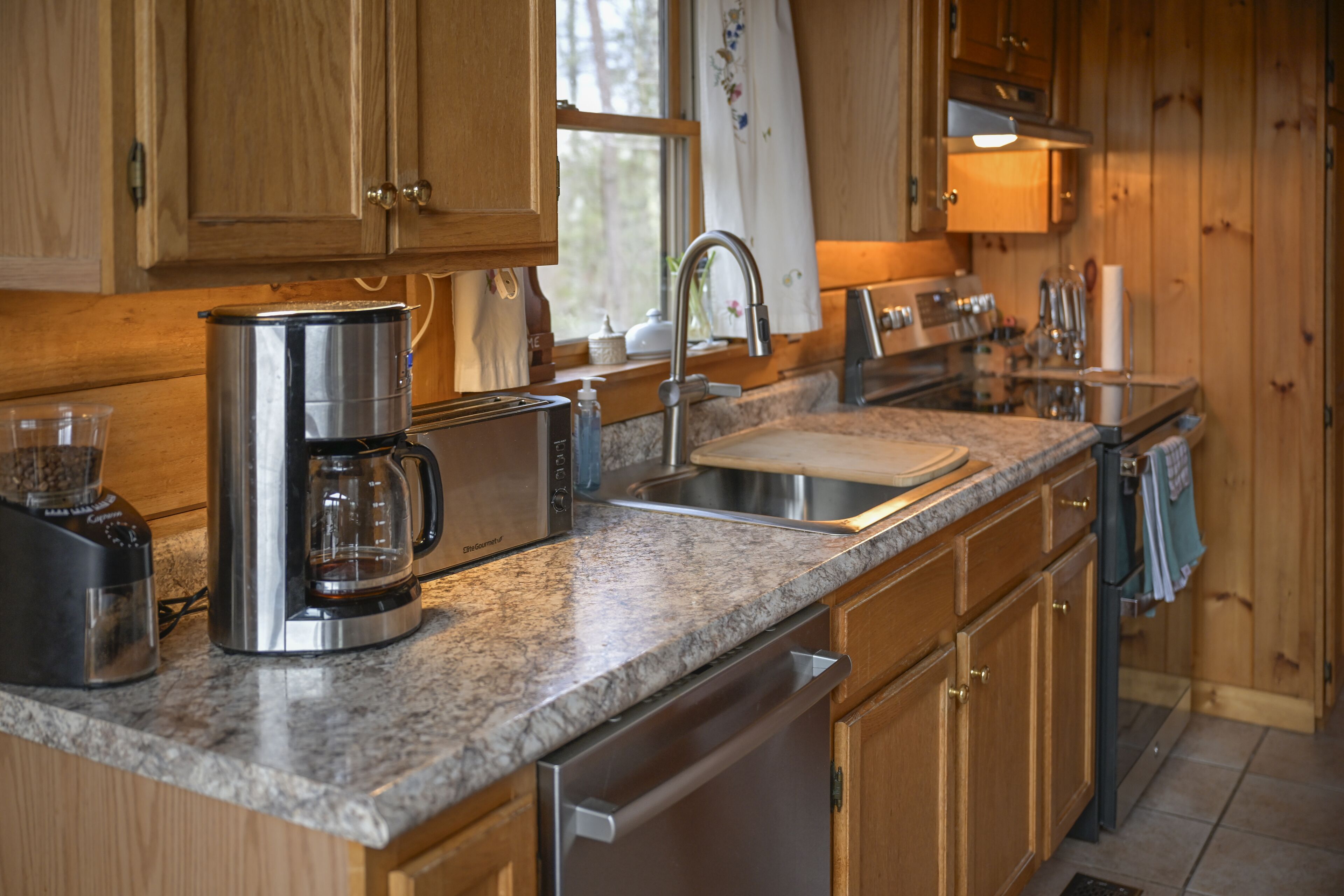 A kitchen with wooden cabinets, a granite countertop, a coffee maker, a toaster, a sink, and a dishwasher.
