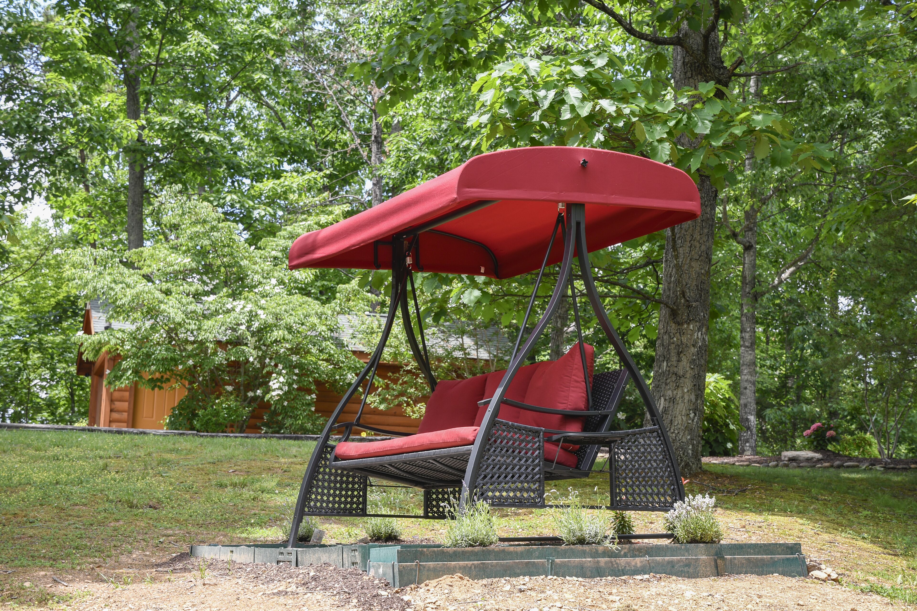Ein roter Schaukelstuhl mit Baldachin in einem Garten.