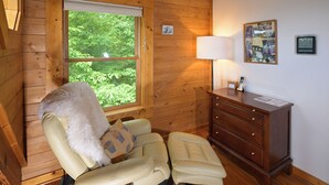A cozy room with a wooden interior, a window with a view of greenery, a lamp, and a wooden dresser. - Trollhaugen—Enjoy Spring and Summer in the Great Smoky Mountains (Sevierville)