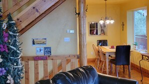 A spacious living area with a black leather sofa, a wooden staircase, and a dining area with a wooden table and chairs.