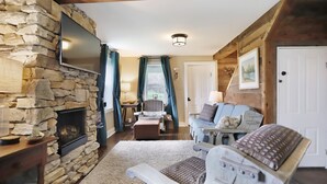 A cozy living room with a stone fireplace, comfortable seating, and a television mounted on the wall. - Near Whitetail, Berkeley Springs, Mercersburg, Hagerstown, Antietam, Frederick (Big Cove Tannery)