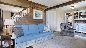 A cozy living room with a blue sofa, a wooden staircase, and a white door. - Near Whitetail, Berkeley Springs, Mercersburg, Hagerstown, Antietam, Frederick (Big Cove Tannery)