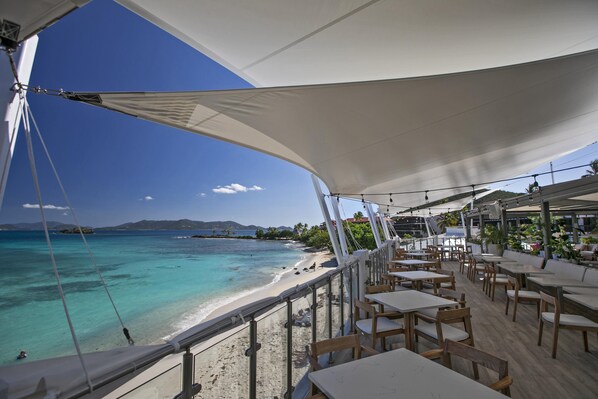 A seaside restaurant with outdoor seating overlooking a beach and ocean.