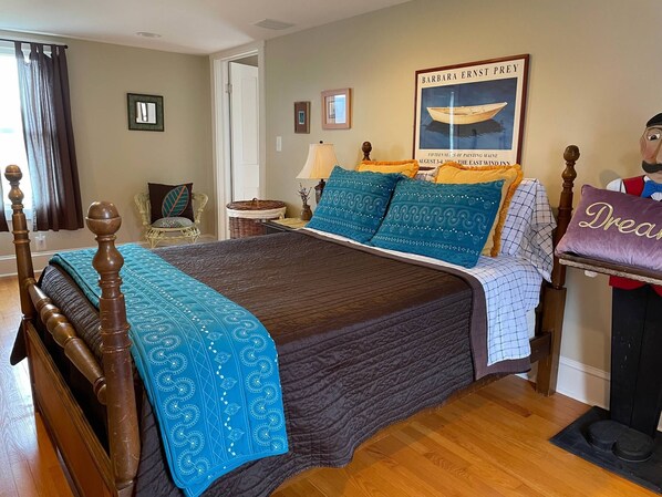 A bedroom with a wooden four-poster bed, a framed painting, a lamp, and a plush toy.