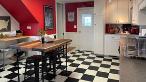 Una cocina con pared roja, piso a cuadros blanco y negro, y gabinetes blancos.