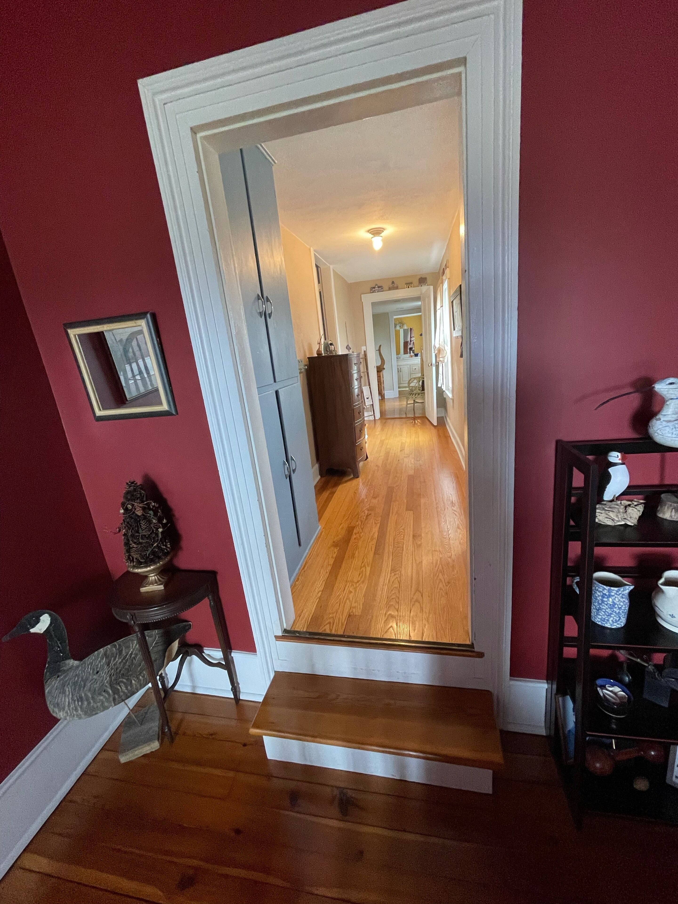 Un couloir doté d’un plancher en bois, un escalier menant à une autre pièce et une étagère ornée d’objets décoratifs.