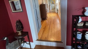 Un pasillo con piso de madera, una escalera que conduce a otra habitación y un estante con objetos decorativos.