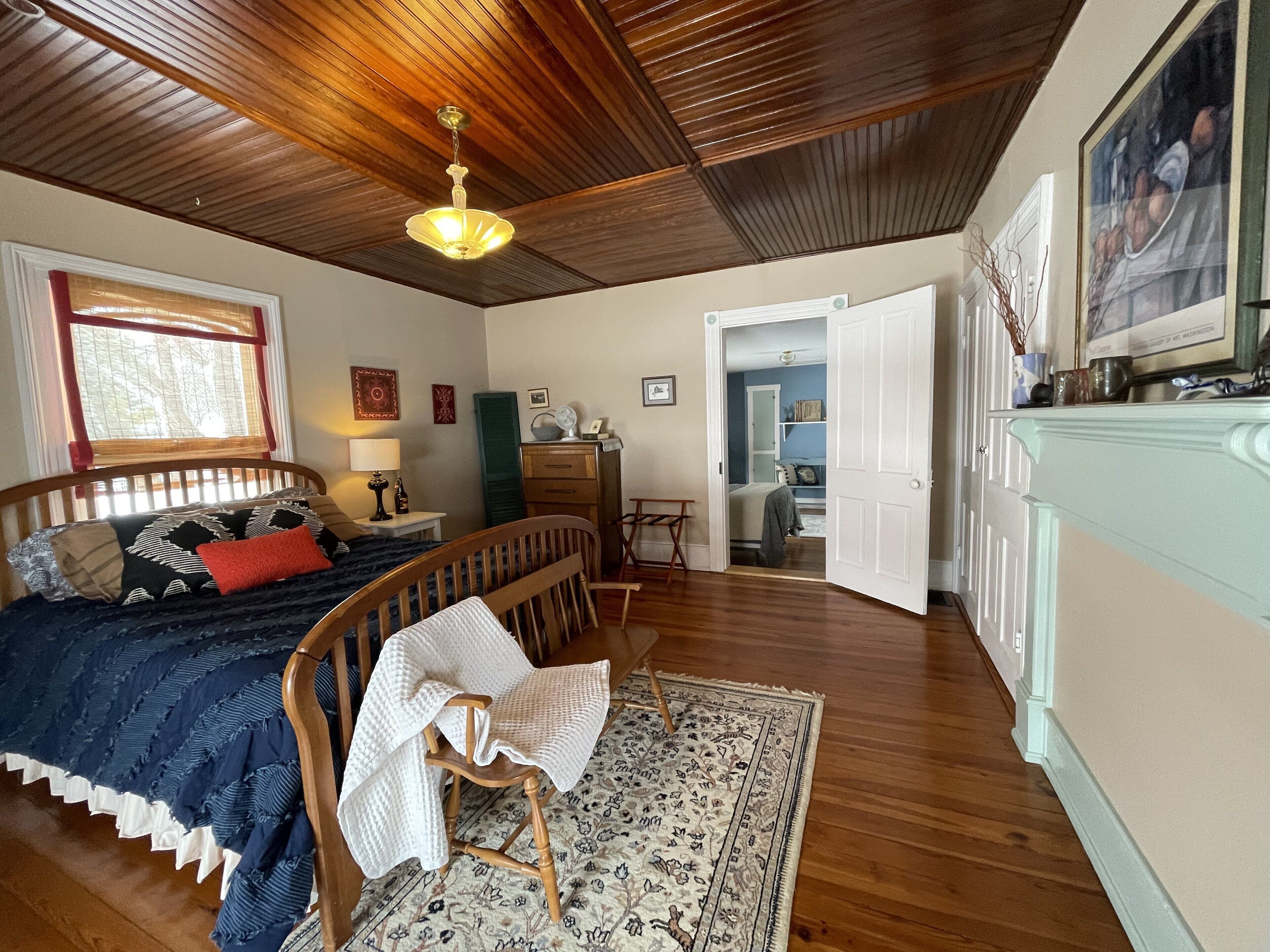 Une chambre avec un plafond en bois, un lit recouvert d’une courtepointe bleue et blanche, une chaise en bois, un bureau et une commode.
