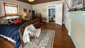 Un dormitorio con techo de madera, una cama con colcha azul y blanca, una silla de madera, un escritorio y un aparador.