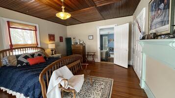 Une chambre avec un plafond en bois, un lit recouvert d’une courtepointe bleue et blanche, une chaise en bois, un bureau et une commode.
