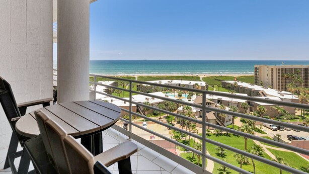 Ein Balkon mit Tisch und Stühlen mit Blick auf einen Strand und einen Ferienort.