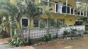A yellow building with a balcony, a white fence, and a gravel driveway.