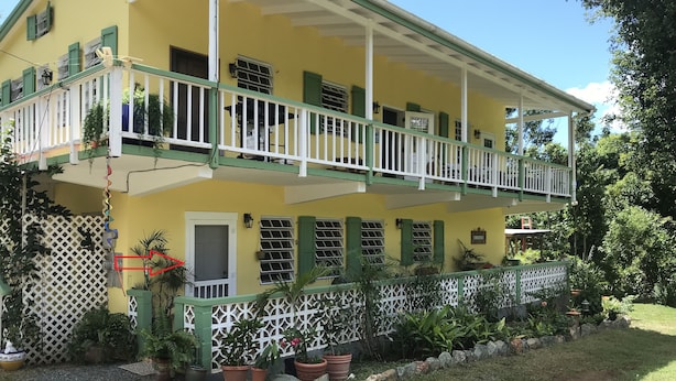 A two-story building with a balcony, potted plants, and a white fence.